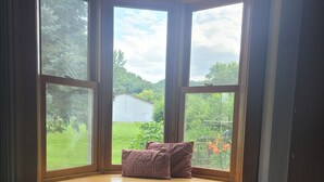Ein Zimmer mit Erkerfenster, das auf eine grüne Landschaft und ein Gewässer blickt.