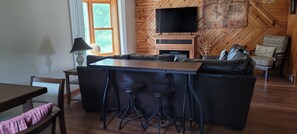 A cozy living area with a wooden wall, a flat-screen TV, a sofa, a coffee table, and a bar stool.