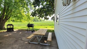 Eine Terrasse mit Picknicktisch und Grill, umgeben von Bäumen und einer Wiese.