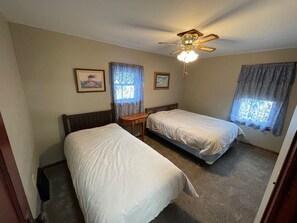 A bedroom with two single beds, a ceiling fan, and two windows with curtains.