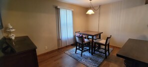 A dining area with a wooden table and four chairs, a patterned rug, and a hanging light fixture.