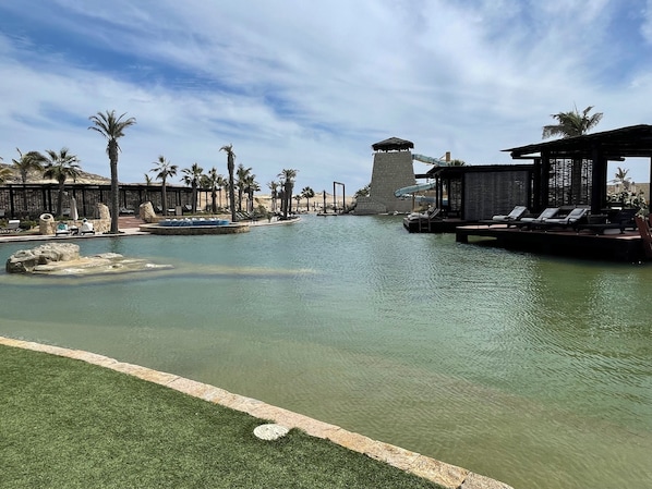 A resort pool area with palm trees, lounge chairs, and a water slide.