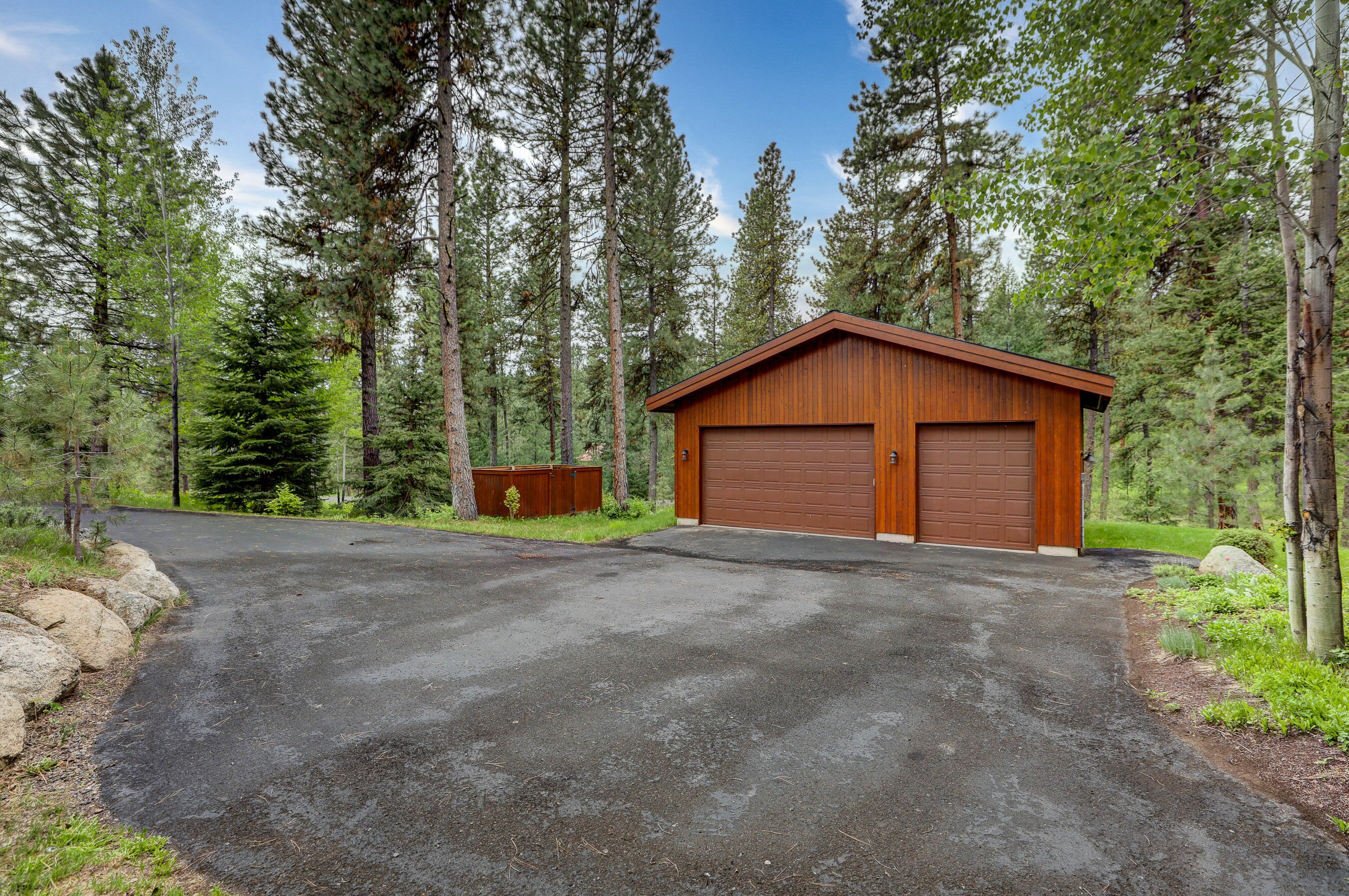 A two-car garage with a wooden exterior, surrounded by a forested area with tall trees.