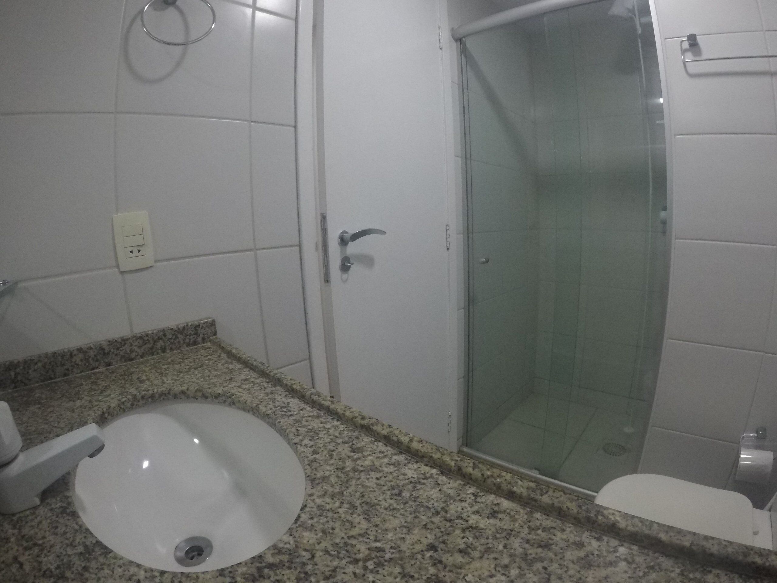 A bathroom with a granite countertop, a white sink, a glass shower enclosure, and a toilet.