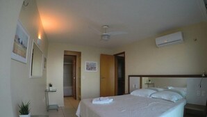 A hotel room with a bed, a ceiling fan, an air conditioning unit, a small table with a plant, and a door leading to another room. - Terraços do Atlântico By Solemar (Fortaleza)