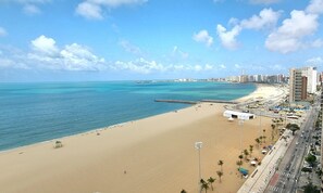 A beach with a sandy shore, a clear blue sea, and a cityscape in the background. - Terraços do Atlântico By Solemar (Fortaleza)