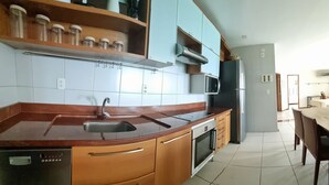 Cocina con encimera curva, pileta de acero inoxidable, horno integrado, microondas y lavavajillas.
