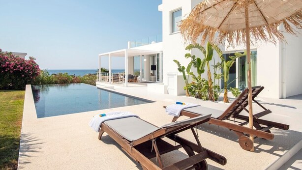 A modern poolside area with lounge chairs, a thatched umbrella, and a view of the sea. - Villa Iolande - Seafront villa with pool in Sicily (Fontane Bianche)