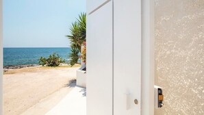 A coastal view with a sandy beach, a clear blue sky, and a white building with a door. - Villa Iolande - Seafront villa with pool in Sicily (Fontane Bianche)
