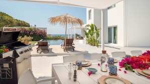 An outdoor dining area with a view of the sea, a grill, and lounge chairs. - Villa Iolande - Seafront villa with pool in Sicily (Fontane Bianche)