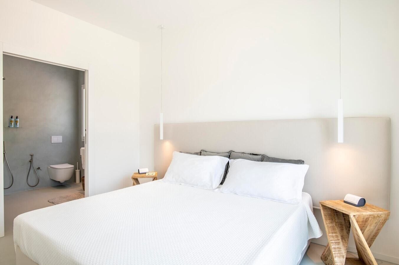 A modern bedroom with a large bed, bedside tables, a nightstand, and a bathroom visible through an open door.