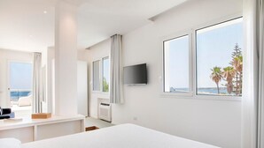 A modern hotel room with a large bed, a desk with a chair, a flat-screen TV, and a view of the sea. - Villa Iolande - Seafront villa with pool in Sicily (Fontane Bianche)