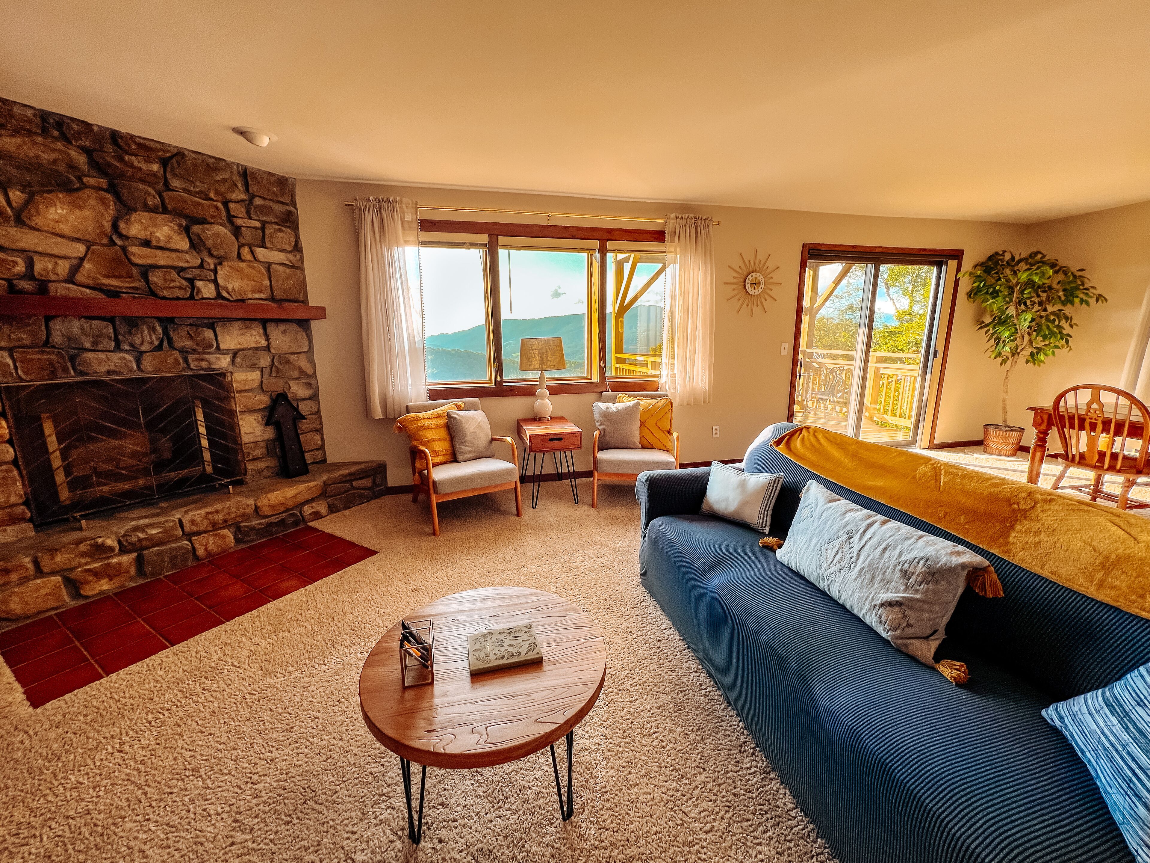 A cozy living room with a stone fireplace, a sofa, a coffee table, and a view of the outdoors.