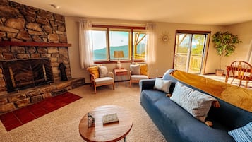 A cozy living room with a stone fireplace, a sofa, a coffee table, and a view of the outdoors.