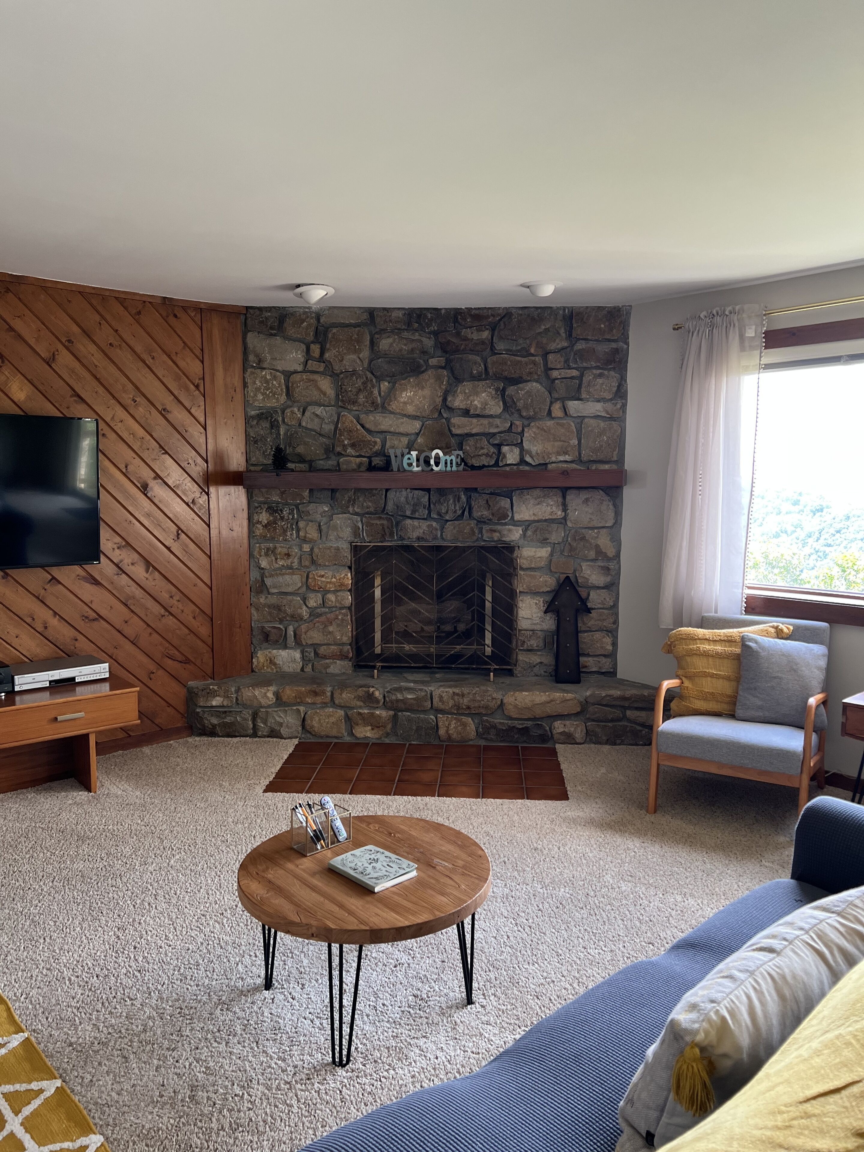 A living room with a stone fireplace, a flat-screen TV, a wooden TV stand, a coffee table, and a sofa.