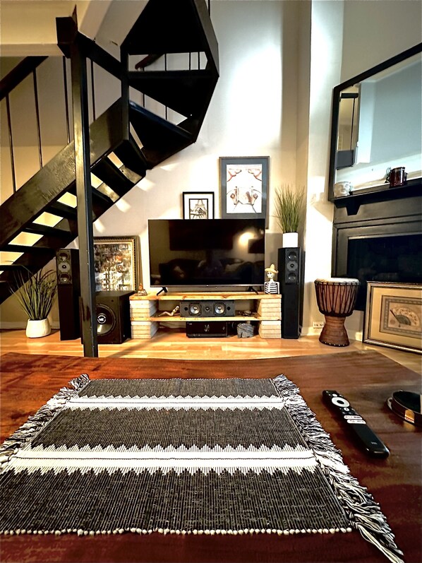 A modern living room with a staircase, a flat-screen TV, speakers, and a fireplace.