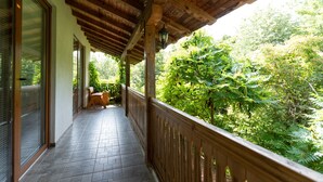 Ein überdachter Balkon mit Holzgeländer und Blick auf einen üppigen Garten.