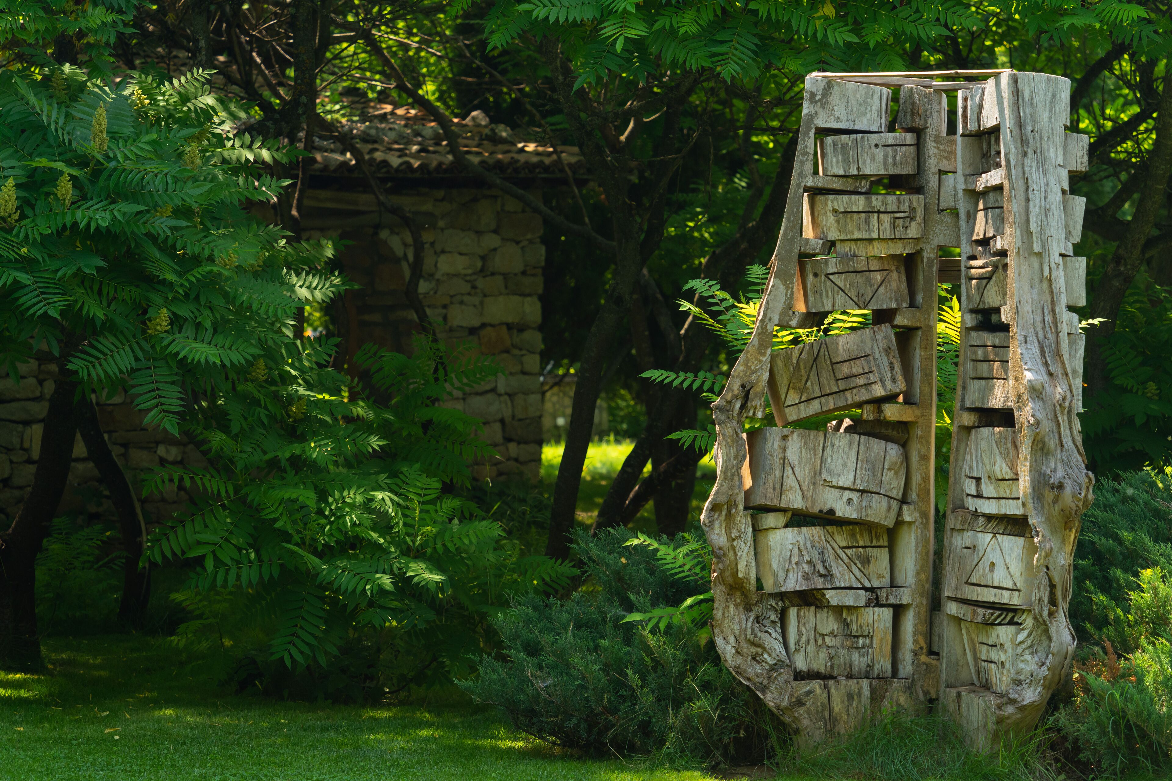 A wooden sculpture in a garden with stone walls and green foliage in the background.