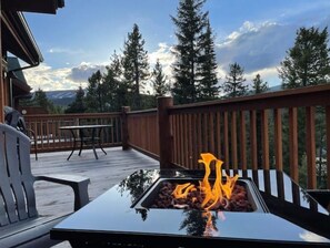 A deck with a barbecue grill, outdoor furniture, and a view of trees and mountains.