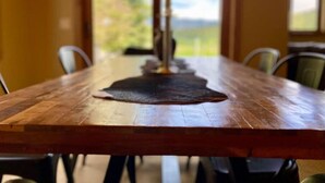 A wooden dining table with chairs, a central decorative item, and a view of a green landscape through a window. - Stunning Mountain View Home, steps to Town Center (Big Sky)