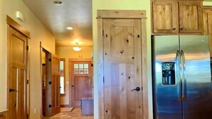 A kitchen with wooden cabinets, a stainless steel refrigerator, and a hallway with wooden doors. - Stunning Mountain View Home, steps to Town Center (Big Sky)