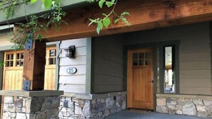 A two-story house with a stone foundation, wooden siding, and a front porch with steps leading to a wooden door. - Stunning Mountain View Home, steps to Town Center (Big Sky)