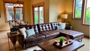 A spacious living room with a large brown leather sectional sofa, a wooden coffee table, and a dining area with a table and chairs. - Stunning Mountain View Home, steps to Town Center (Big Sky)