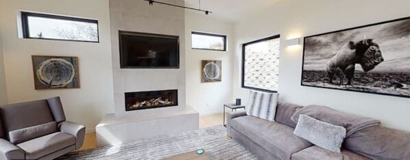 Una sala de estar moderna con chimenea, un sofá gris y un cuadro abstracto grande en la pared.
