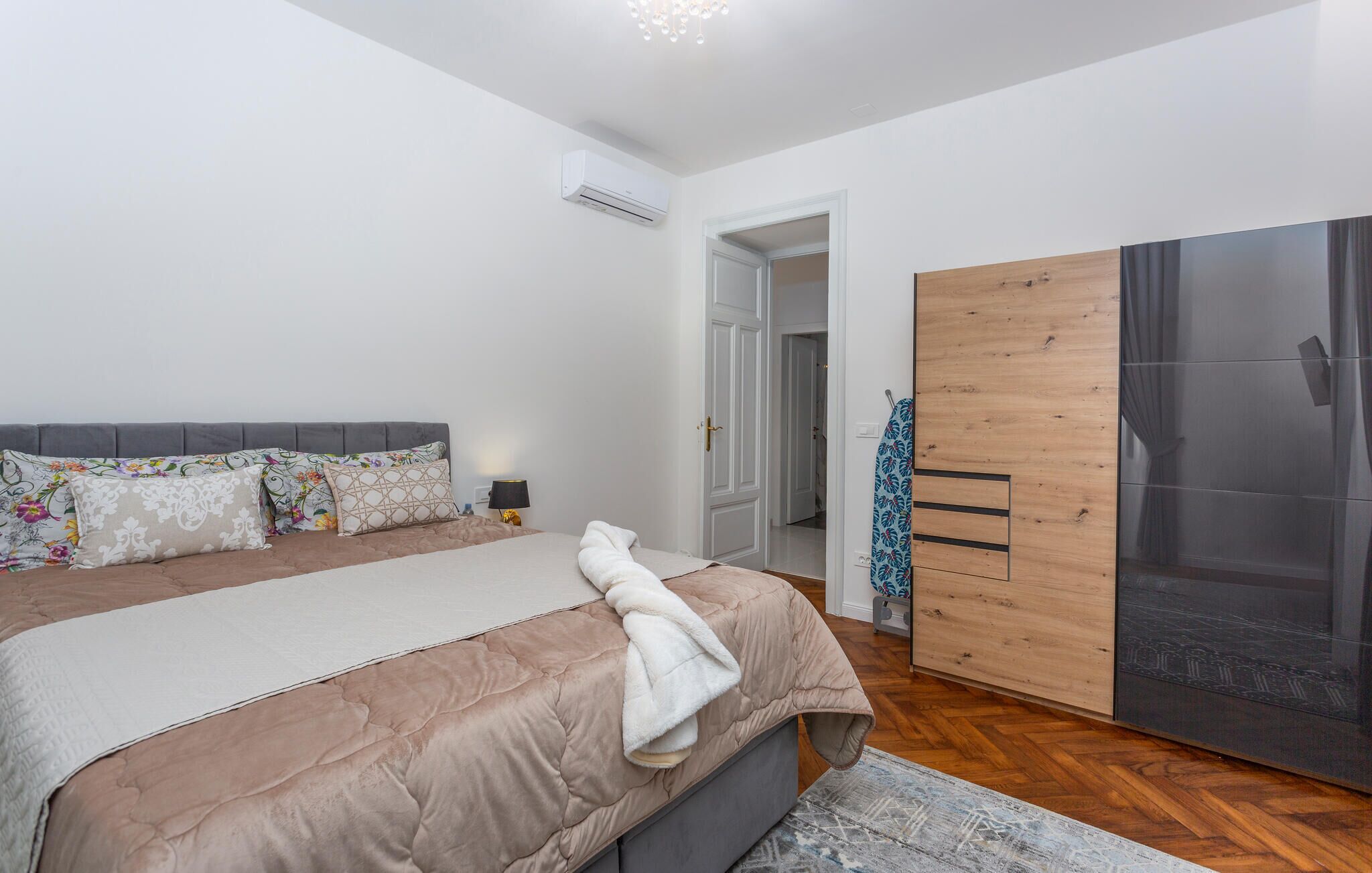 Ein Schlafzimmer mit Bett, Nachttisch, Lampe, Kleiderschrank und einer offenen Tür zu einem anderen Raum.