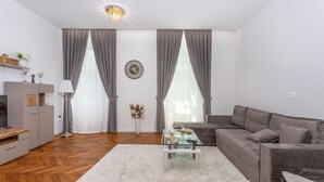 A modern living room with a grey sofa, a glass coffee table, and a wooden herringbone floor.