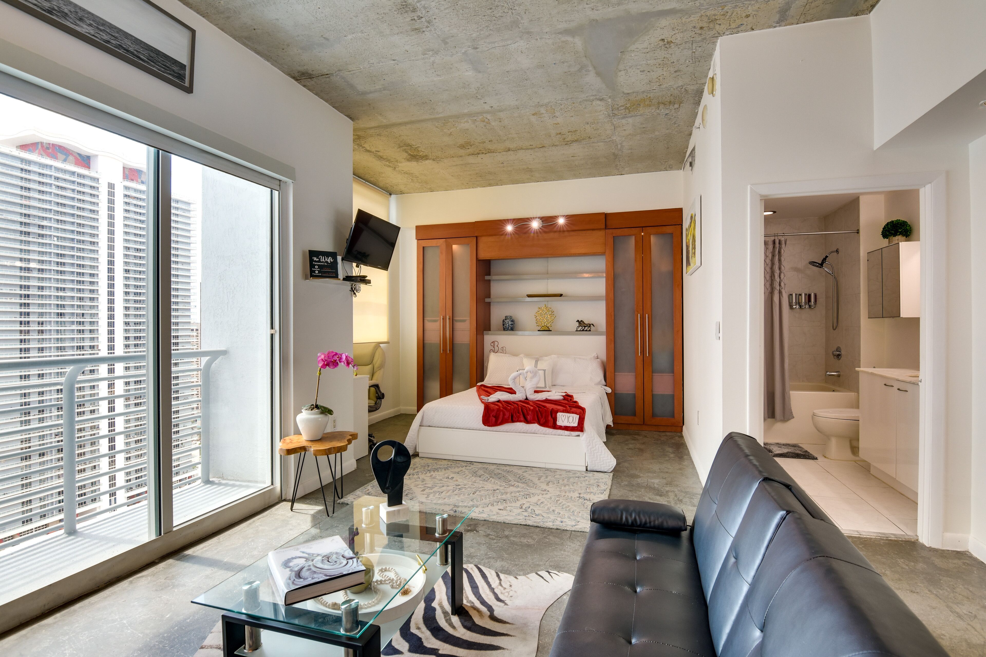 Ein modernes Schlafzimmer mit großem Fenster, einem Glastisch, einer schwarzen Ledersofa und einem Holzschrank.