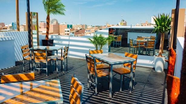 Una terraza al aire libre con mesas y sillas, plantas en macetas y vistas a la ciudad.