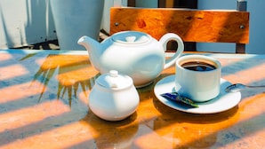 Una mesa con una tetera, una taza, un plato y dos plantas en macetas.