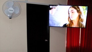 Una habitación con una cama, un televisor montado en la pared y un ventilador de techo.