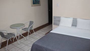 Una habitación de hotel con cama, dos sillas, una mesita y un cuadro en la pared.