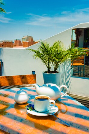 Ein Tisch mit Teekanne, Tasse und Untertasse, einer Topfpflanze und Gebäuden im Hintergrund.