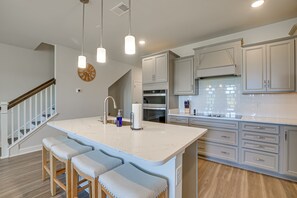 A modern kitchen with a large island, wooden bar stools, and light gray cabinets. - Golf Getaway w/ Pool Access in North Myrtle Beach (North Myrtle Beach)