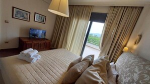 Une chambre d’hôtel avec un grand lit, un téléviseur posé sur une commode en bois et une vue sur l’extérieur grâce à une grande fenêtre.