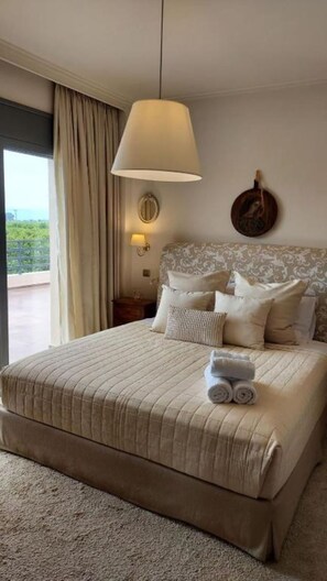 Une chambre avec un grand lit, une lampe suspendue, une vue sur l’extérieur et une assiette décorative accrochée au mur.