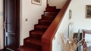 Un escalier avec des marches en bois et une rampe, menant à un palier où se trouvent un tableau encadré et un vase contenant des plantes séchées.