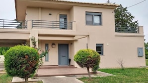 Une maison à deux étages avec un balcon, une porte d’entrée et deux petits arbres dans le jardin.