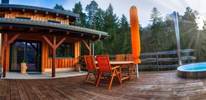 A wooden deck with a hot tub, outdoor seating, and a covered area with a table and chairs.