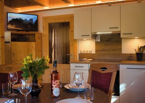 A dining area with a table set for two, a bottle of wine, and a television mounted above the door. - Vacation home with panoramic terrace and whirlpool in a sandstone idyll (Rathen)