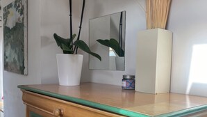 Une commode en bois avec des bordures vertes et trois tiroirs, un vase blanc avec des fleurs blanches, un miroir et un petit récipient posé sur le dessus.