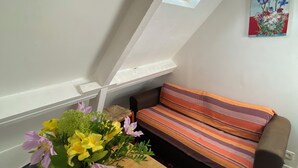 Une pièce avec un plafond en pente, une table en bois sur laquelle est posé un vase de fleurs, un canapé à rayures et un tableau accroché au mur.
