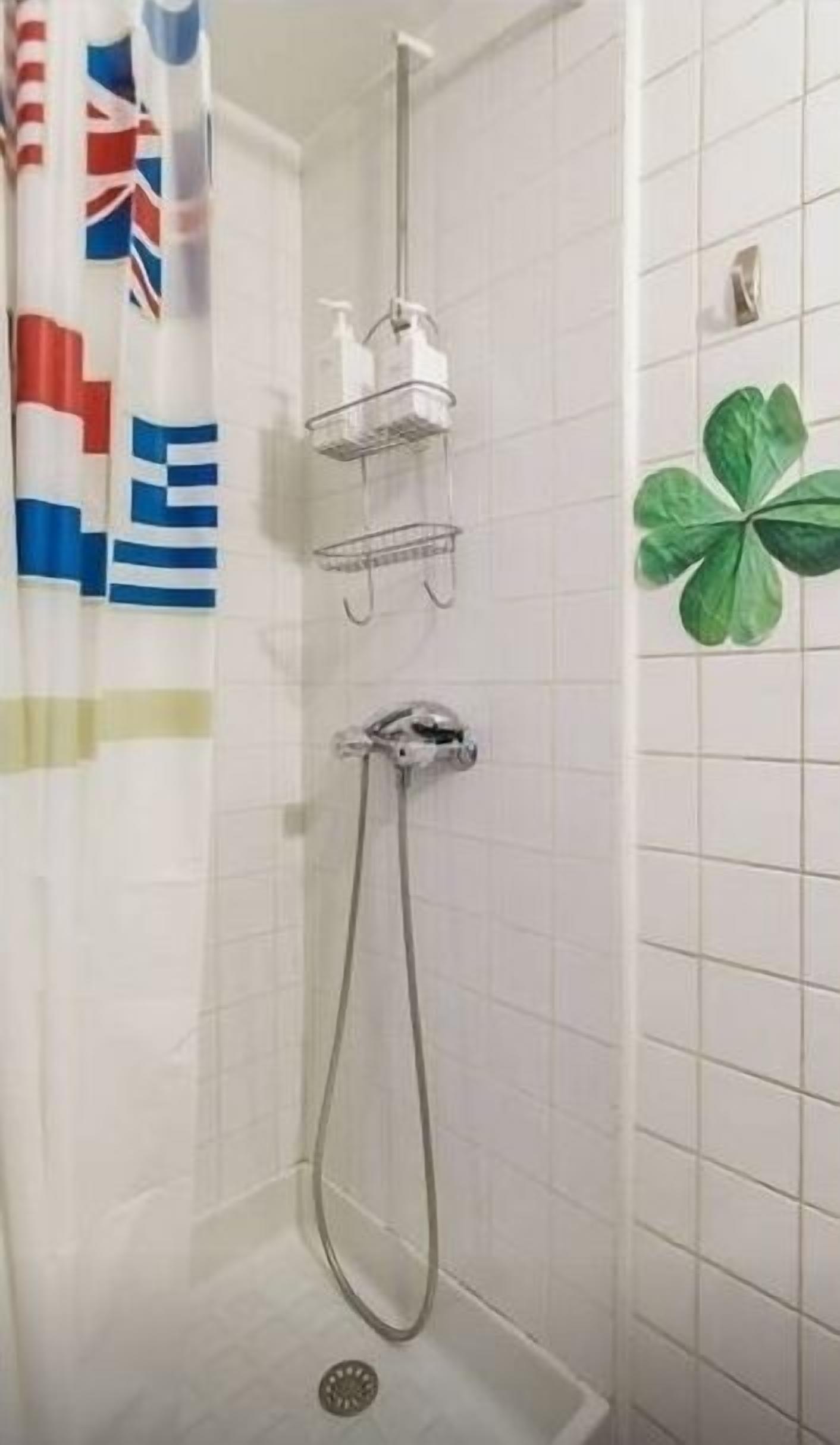 Un espacio de ducha con cabezal, dispensador de jabón y jabonera en un estante fijado a la pared.