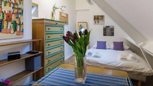 Une chambre à coucher avec un lit, une commode, un vase de fleurs et une fresque colorée sur le mur.