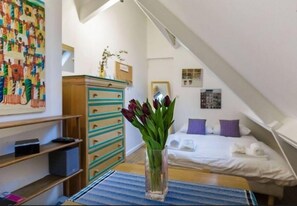 Een slaapkamer met een bed, een dressoir, een vaas met bloemen en een kleurrijke muurschildering.
