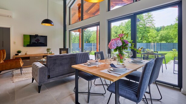 A modern dining area with a wooden table, blue upholstered chairs, and a large window offering a view of the outdoors. - WELLNESS HOUSE BY THE LAKE (Brezova Gora)