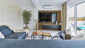A modern living room with a sofa, a coffee table with a chessboard, a potted plant, and a TV mounted on a wooden panel wall. - Beach front home in Bibinje (Bibinje)
